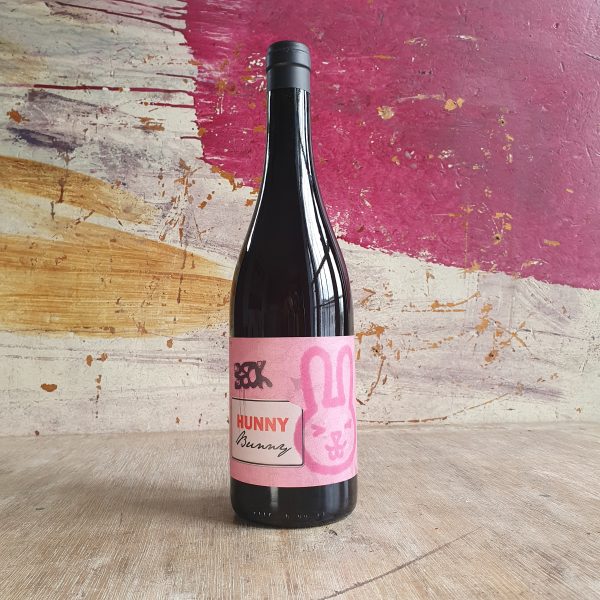 A bottle of 'Hunny Bunny' red wine on a wooden countertop. The label is pink, and features a cartoon bunny with the winemakers name, 'Judith Beck' printed above