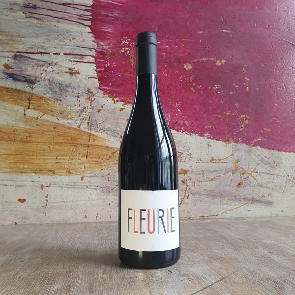 A bottle of red wine made by Karim Vionnet in front of a colourful backdrop. The label is white with 'Fleurie' printed in large multicoloured capital letters
